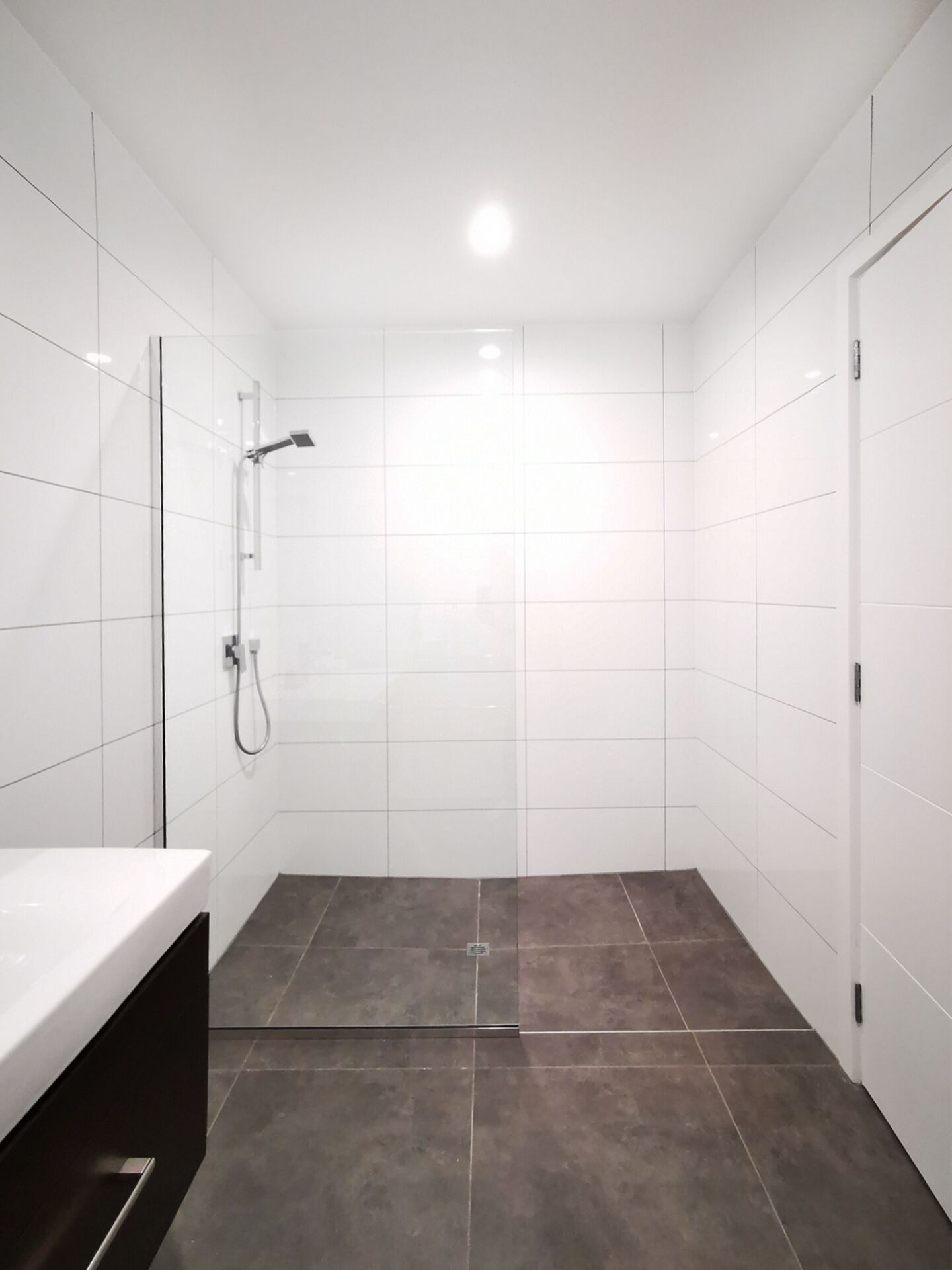 Un baño moderno con azulejos blancos, ducha y suelo oscuro.
