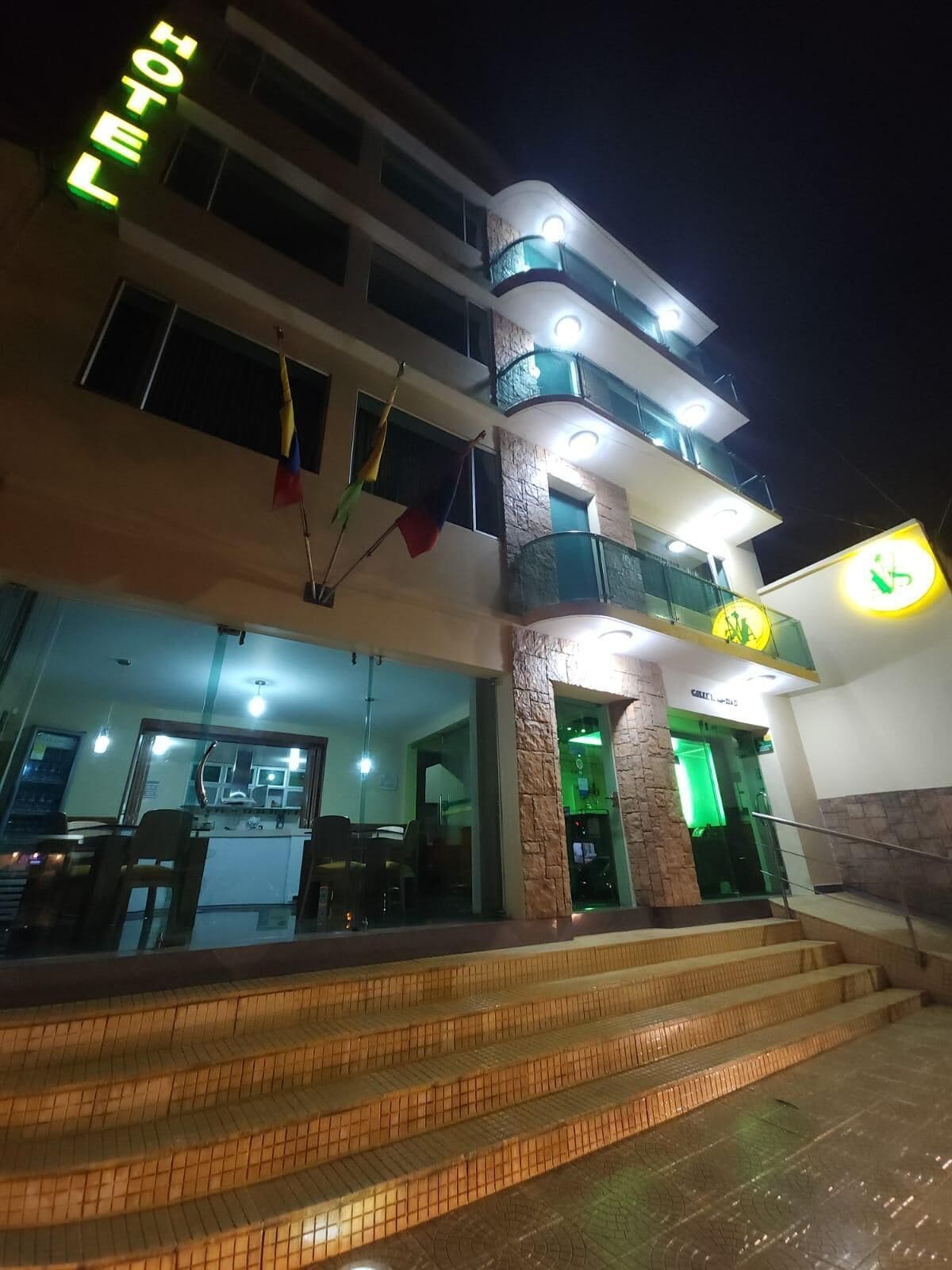 Un hotel con un diseño moderno, que presenta una escalera que lleva a la entrada, un área de recepción visible y un letrero con el nombre del hotel.