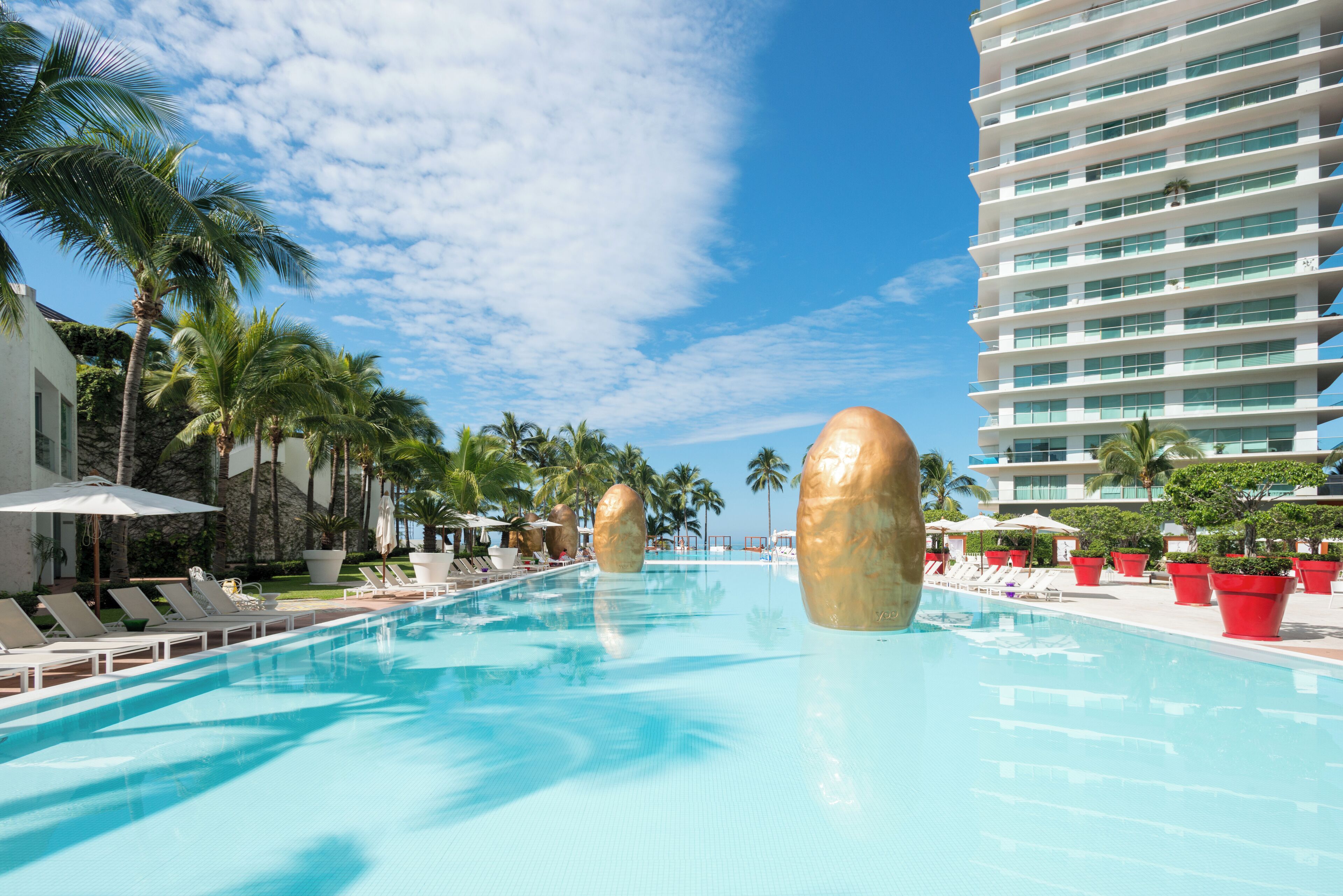 Une piscine entourée de chaises longues et de palmiers, le tout bordé par un grand bâtiment d’hôtel.