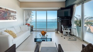 Uma sala de estar moderna com um sofá branco, uma mesa de centro de vidro e uma TV em um suporte.