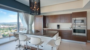 Uma cozinha moderna com ilha central, banquetas, eletrodomésticos de aço inoxidável e vista para a cidade.