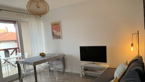 A modern living room with a grey sofa, a TV, a dining table with clear chairs, and a wicker ceiling light. - Apartment T3 with terrace, 100 m from the beach and 5 min by bike from the lake (Soorts-Hossegor)