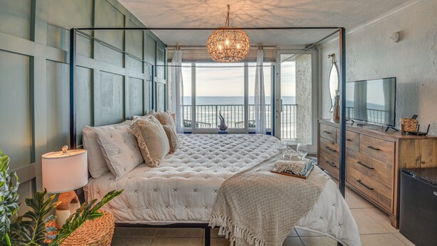 Een slaapkamer met een groot bed, een televisie en uitzicht op zee.