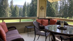 Une terrasse couverte, aménagée avec des meubles en osier, une table en verre et offrant une vue sur un terrain de golf.