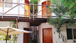 Un patio con una puerta de madera, plantas en macetas, un paraguas blanco y una mesa pequeña.