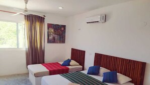 Habitación de hotel con dos camas, ventilador de techo, aire acondicionado y una ventana con cortinas.