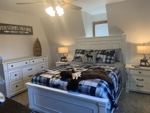 A bedroom with a bed, two bedside tables, a ceiling fan, a wall sign, and a window.