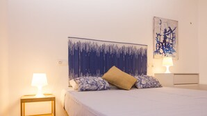 A neatly arranged bedroom with a bed, two bedside tables with lamps, a wall-mounted artwork, and a patterned tapestry. - Casa Alameda Cadiz Centro (Cádiz)