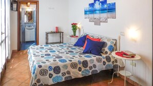 A bedroom with a patterned bedspread, a bedside table with a lamp, and a wall-mounted artwork of a beach scene.