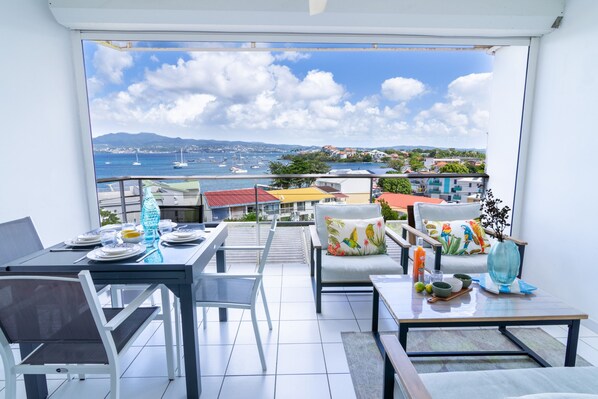 A balcony with a dining setup overlooking a marina and coastal town.