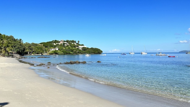 Una playa con agua cristalina, barcos y una casa en una colina.