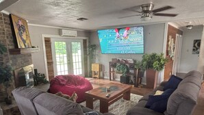 Una sala de estar con televisor, chimenea, sofá, mesa de centro y planta.