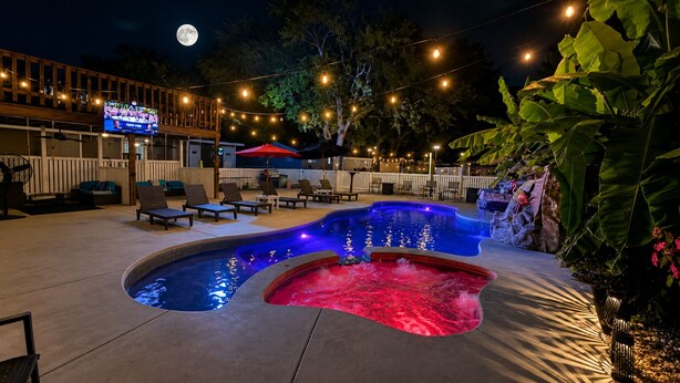 Un área de piscina con hidromasaje, sillas de descanso e iluminación colgante.