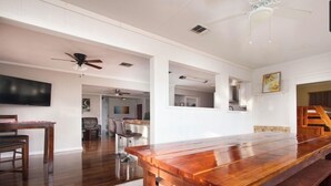 Un comedor amplio con una mesa de madera larga y sillas, un ventilador de techo y un televisor montado en la pared.