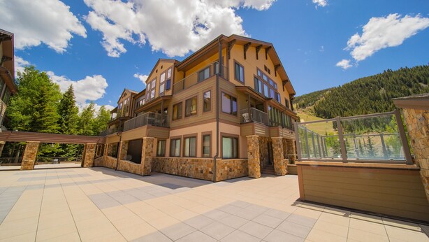 A multi-story building with a balcony, stone pillars, and a view of a forested hillside. - Slopeside 2762 (Keystone)
