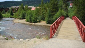 A wooden bridge leading to a lodge surrounded by dense forest and a river. - Slopeside 2762 (Keystone)