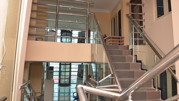 Interior moderno de un hotel con una escalera de cristal que conecta dos plantas, un extintor visible y una vista del área de recepción.