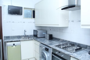 Eine Küche mit weißen Schränken, einem Geschirrspüler, einer Waschmaschine, einer Mikrowelle, einem Toaster und einem Gasherd.
