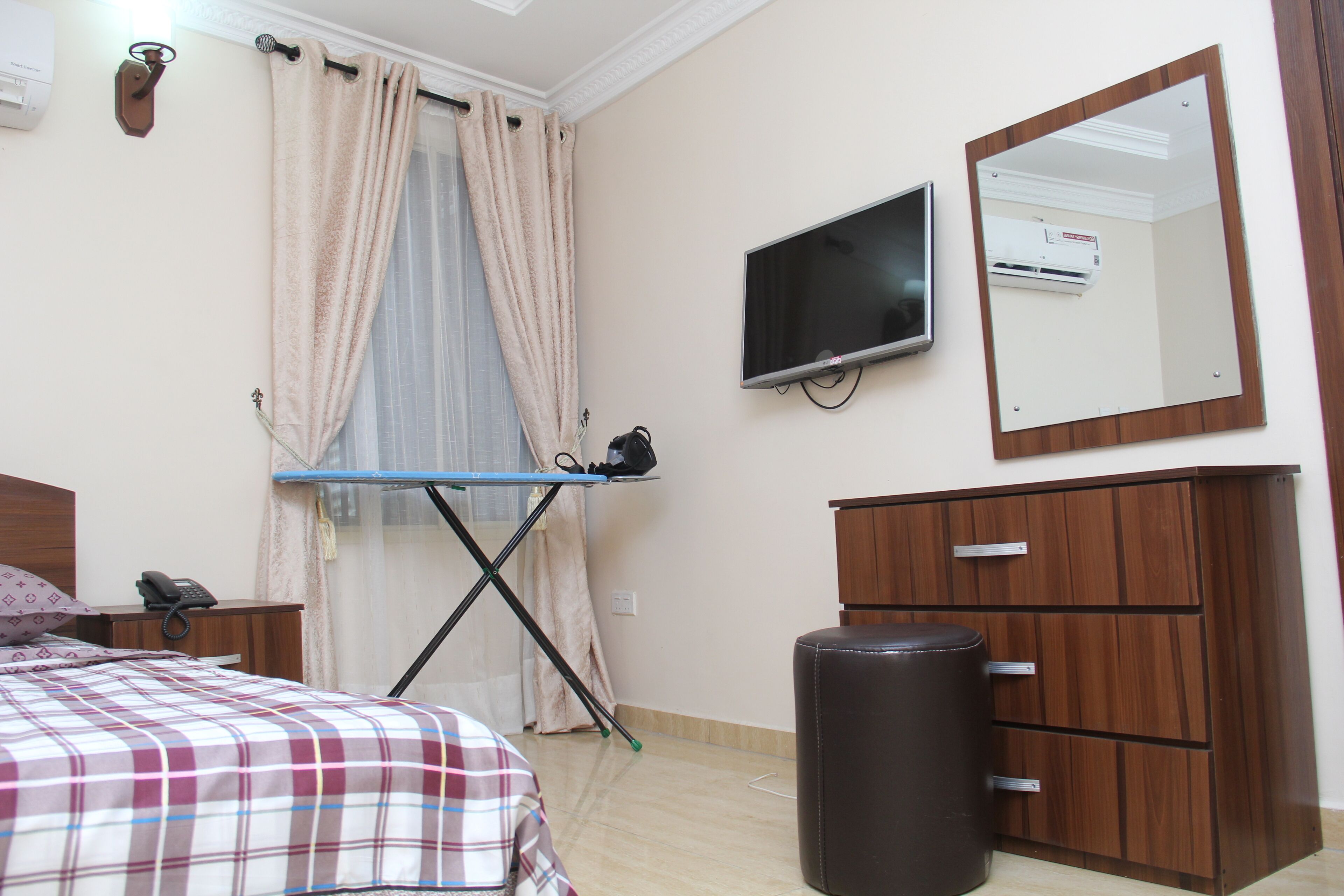 Um quarto com cama, escrivaninha com cadeira, televisão, espelho e guarda-roupa.