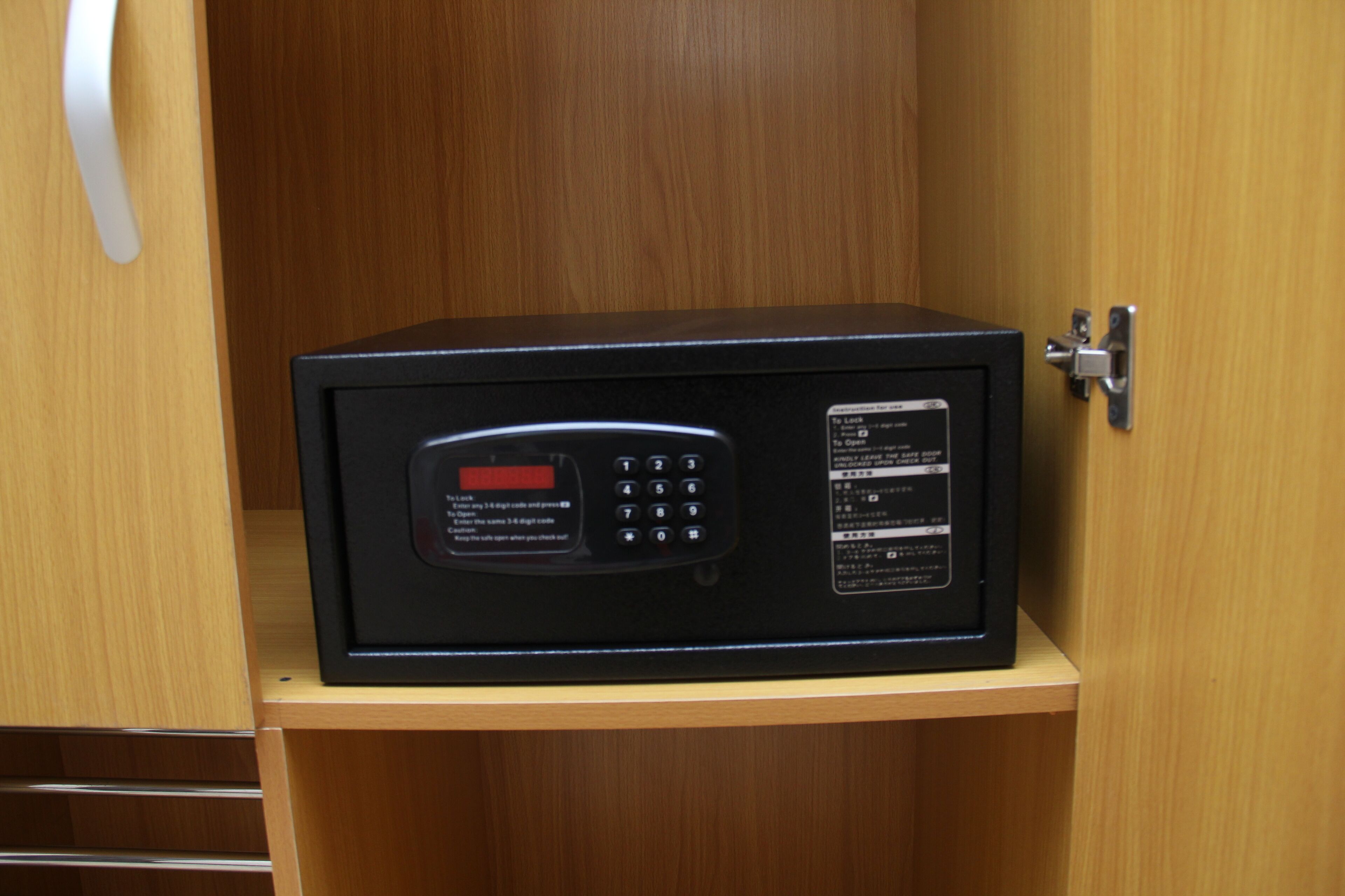 A black safe with a keypad and instructions on a wooden shelf.