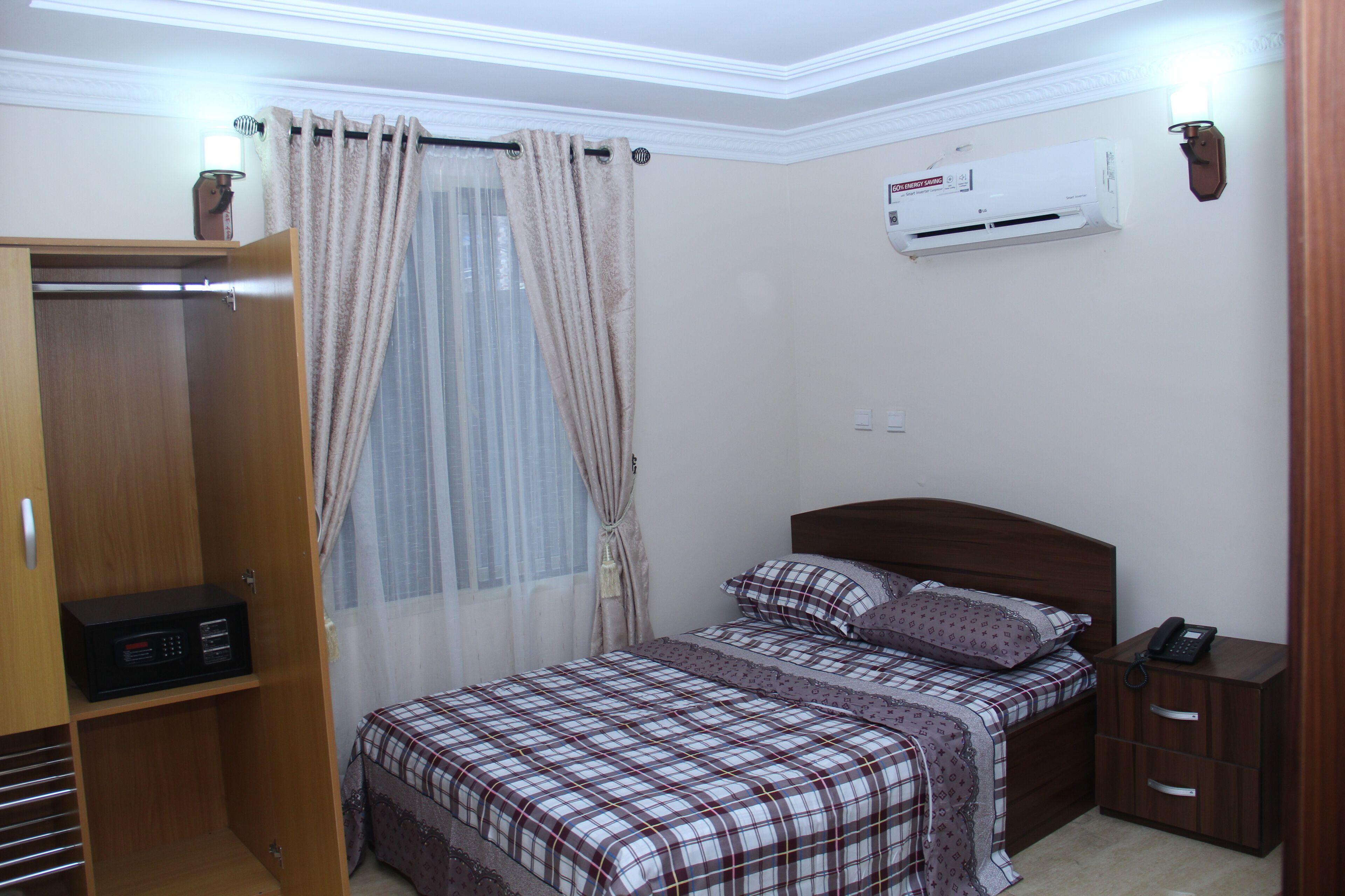A bedroom with a bed, a wardrobe, a bedside table, and an air conditioning unit.