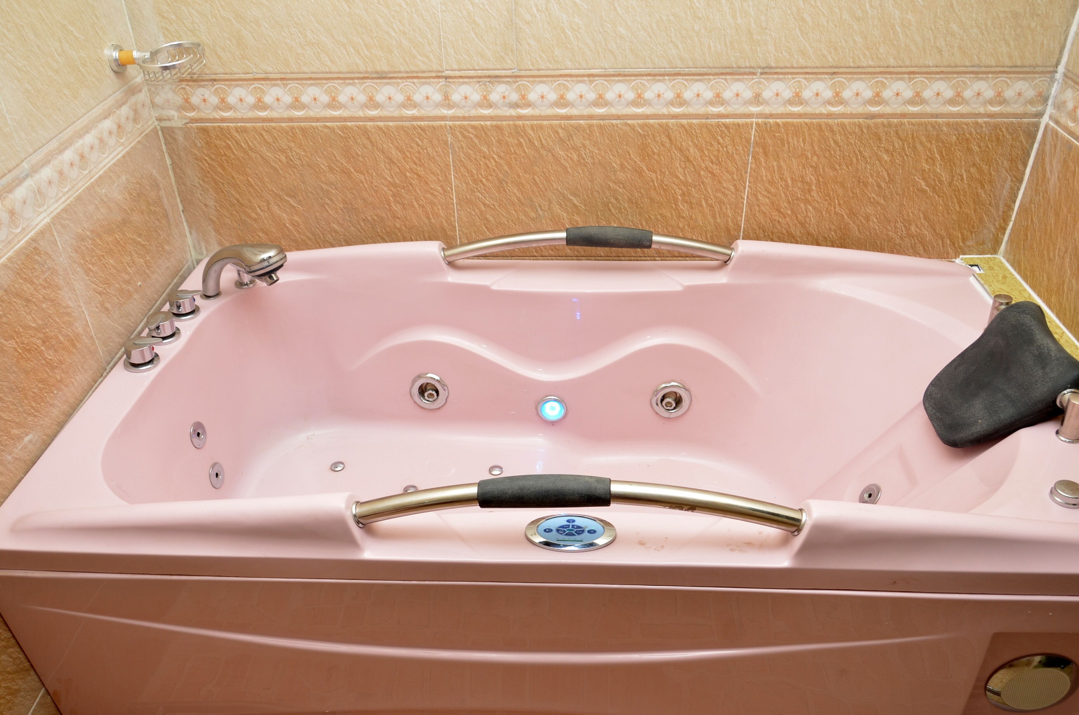 A pink jacuzzi tub with a control panel, a handheld showerhead, and a black towel.