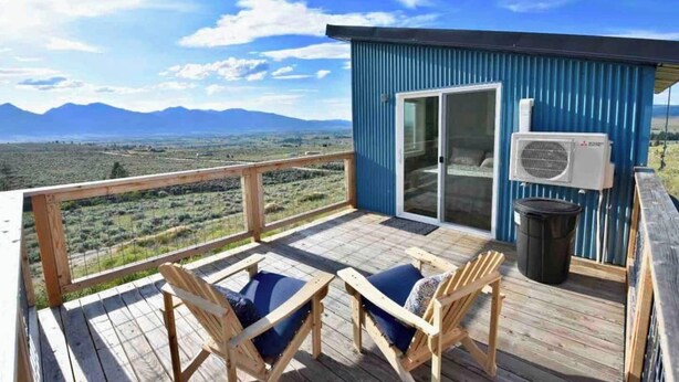 Um terraço com duas cadeiras e uma mesa, com vista para uma paisagem montanhosa.