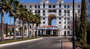 Stunning hotel with a classic arched entrance, surrounded by lush palm trees and a beautifully maintained driveway.