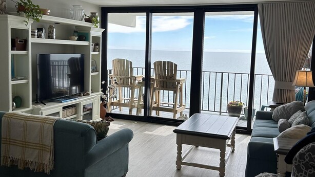 A living room with a TV, sofas, a coffee table, and a view of the sea through large windows. - Stunning Royal Garden Unit 1002 (Murrells Inlet)