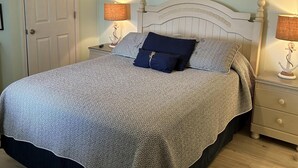 A bedroom with a bed, two bedside tables, a ceiling fan, a door, and a painting on the wall. - Stunning Royal Garden Unit 1002 (Murrells Inlet)