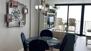 A dining area with a round table, dark chairs, and a chandelier. There is a view of a balcony with chairs and a railing. - Stunning Royal Garden Unit 1002 (Murrells Inlet)