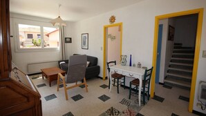 Una sala de estar con sofá, una mesa, una silla, una mesita auxiliar, una lámpara colgante, una ventana y una escalera.