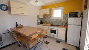 Una cocina compacta con una mesa de comedor, sillas, microondas, horno y pileta.