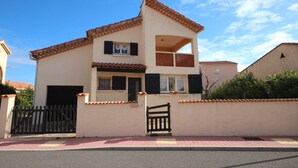 Una casa de dos pisos con techo de tejas, balcón y entrada protegida por una reja.