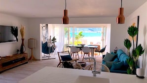 Ein modernes Wohnzimmer mit einem großen weißen Waschbecken, Korbmöbeln und Blick auf den Ozean.