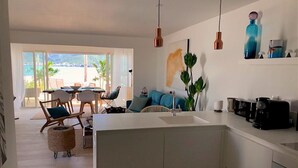 Eine moderne Küche mit Kochinsel, ein Essbereich mit Stühlen und Tisch sowie Meerblick durch große Fenster.