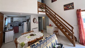 Un comedor con una mesa dispuesta para cuatro, una escalera y una cocina al fondo.