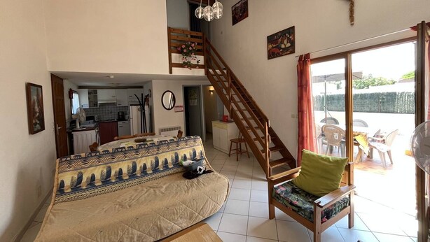 Una sala de estar con sofá, una escalera de madera, un comedor y una cocina al fondo.