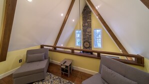 Ein Schlafzimmer im Loft-Stil mit schrägem Dach, Holzbalken, einer Steinwand und zwei grauen Sofas.