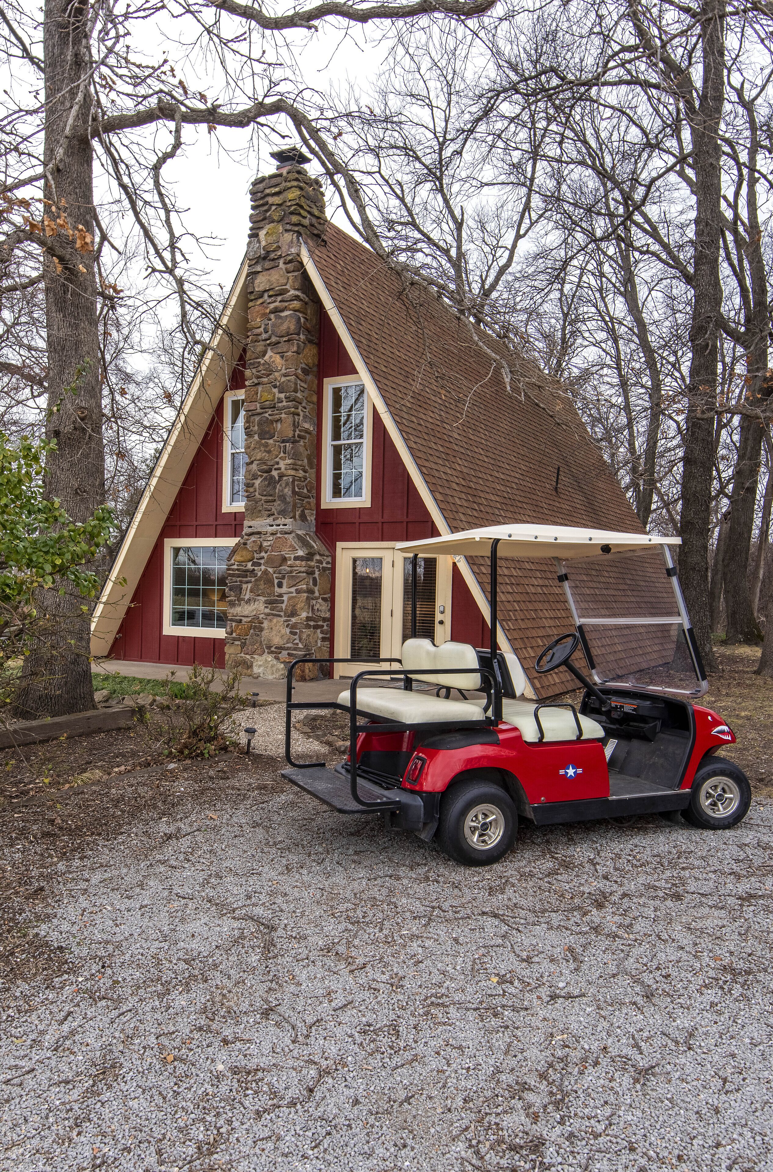 Een rood gebouw met stenen details en een schuin dak, met een golfkar ervoor en bomen op de achtergrond.