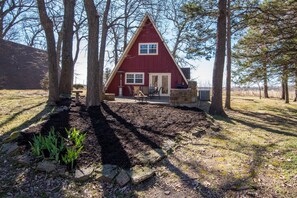 A red triangular cabin with a front porch, surrounded by trees. - Fly-In Home on Monkey Island, Grand Lake OK (Afton)