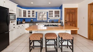 A modern kitchen with white cabinets, a black refrigerator, a wooden island with stools, and a blue accent wall.