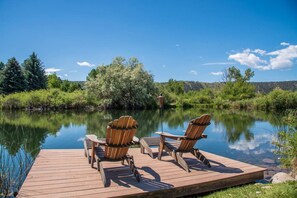 Eine Holzsteg mit zwei Adirondack-Stühlen, die auf einen stillen See blicken, umgeben von üppiger Vegetation und Bäumen.