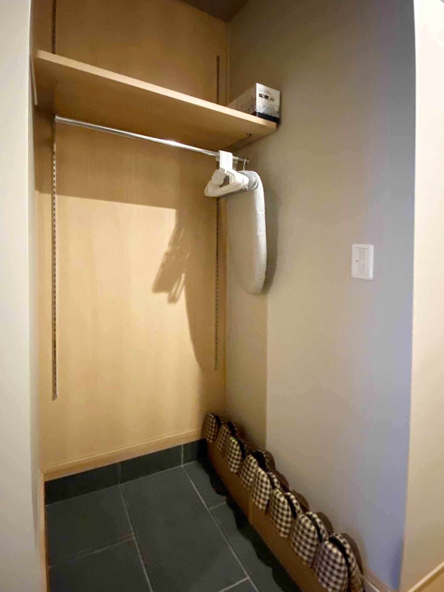 Una habitación pequeña y cerrada con un armario de madera, una toalla colgada en un gancho y una fila de bolsas a cuadros contra la pared.