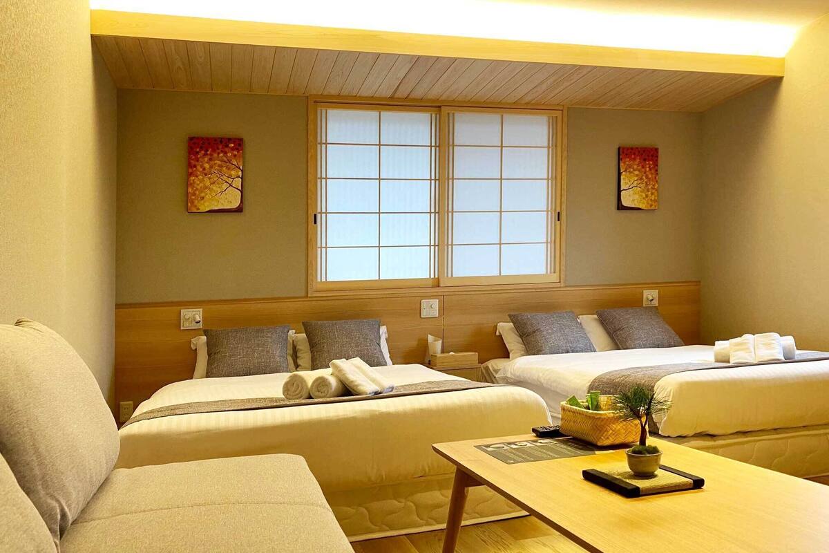 A hotel room with two beds, a sofa, a small table, and a window with a view.