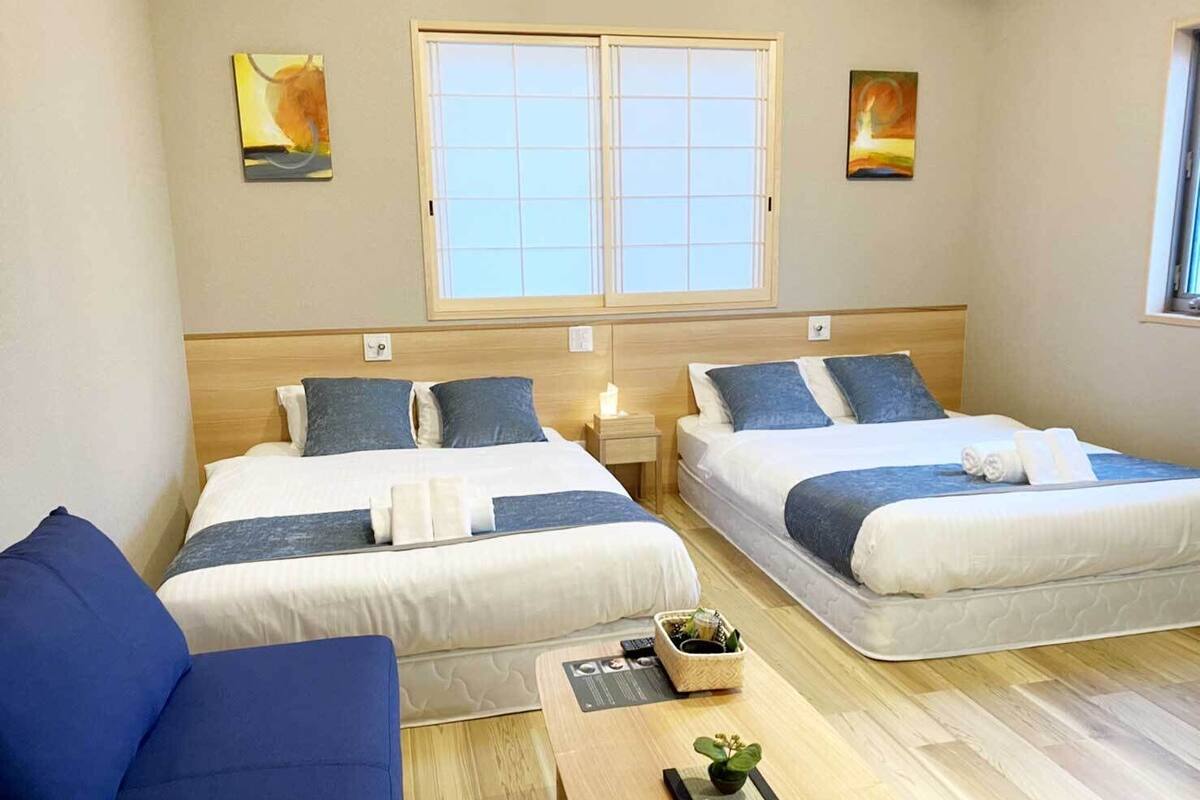 A hotel room with two beds, a sofa, a small table with a plant, and artwork on the walls.