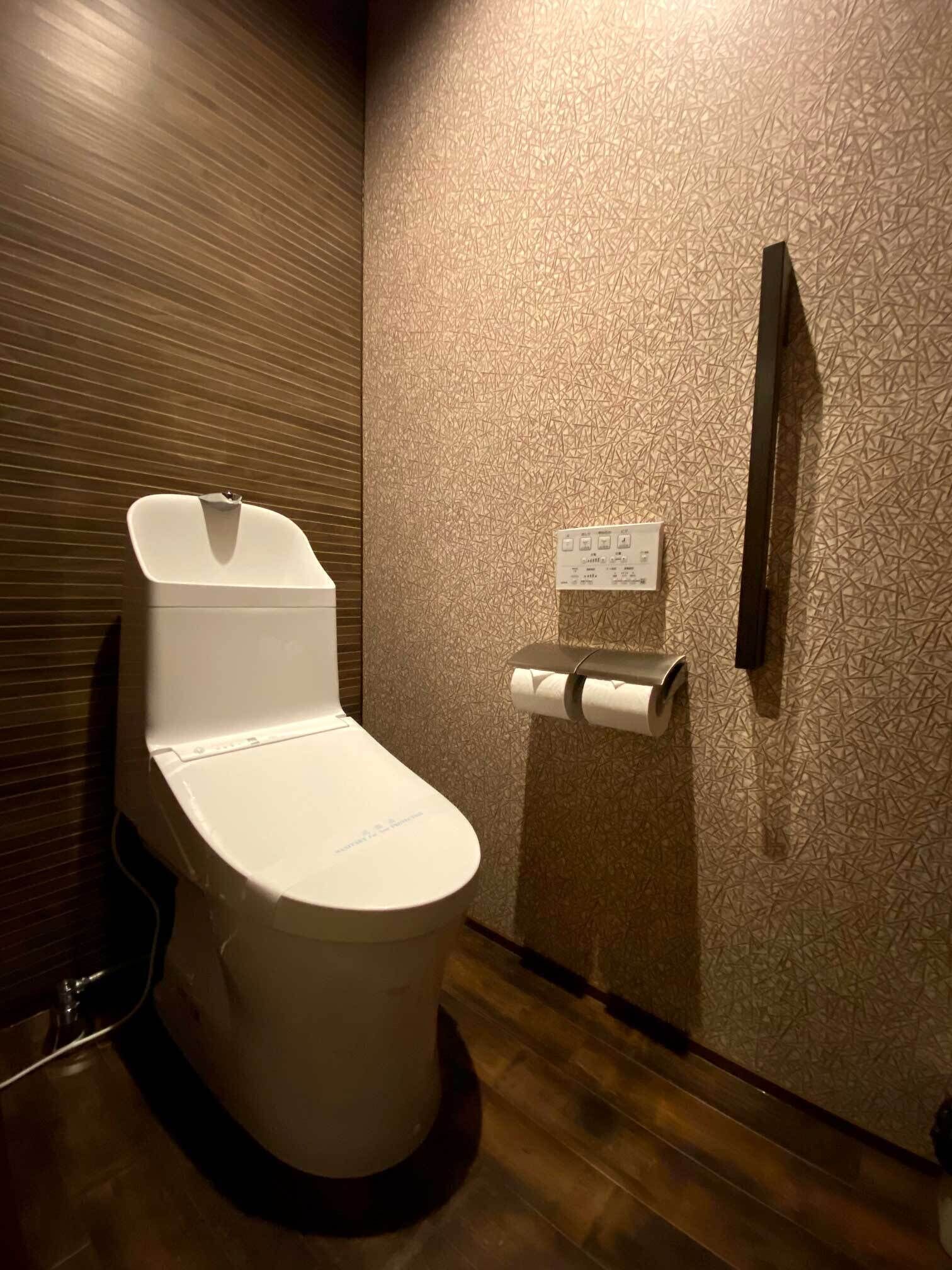A modern bathroom with a toilet, a paper towel dispenser, and a wall-mounted toilet paper holder.