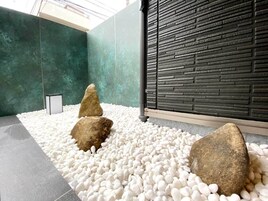 Ein moderner Innenbereich mit Kies, großen Steinen, einer grünen Wand und einer strukturierten schwarzen Wand.