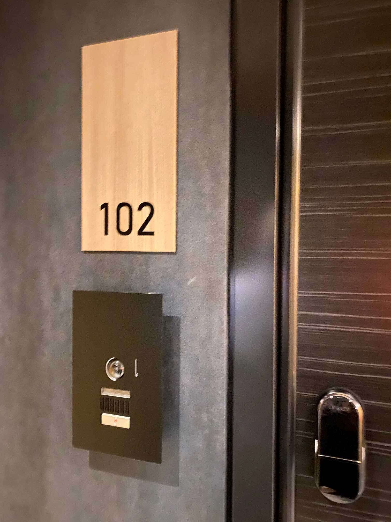 Een deur met een bordje '102' en een gleuf voor een sleutelkaart.