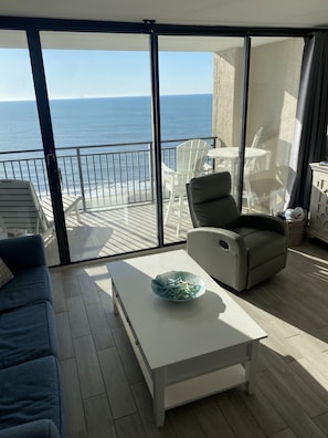 Un balcon avec vue sur la mer, aménagé avec un canapé, un fauteuil et une table à manger.